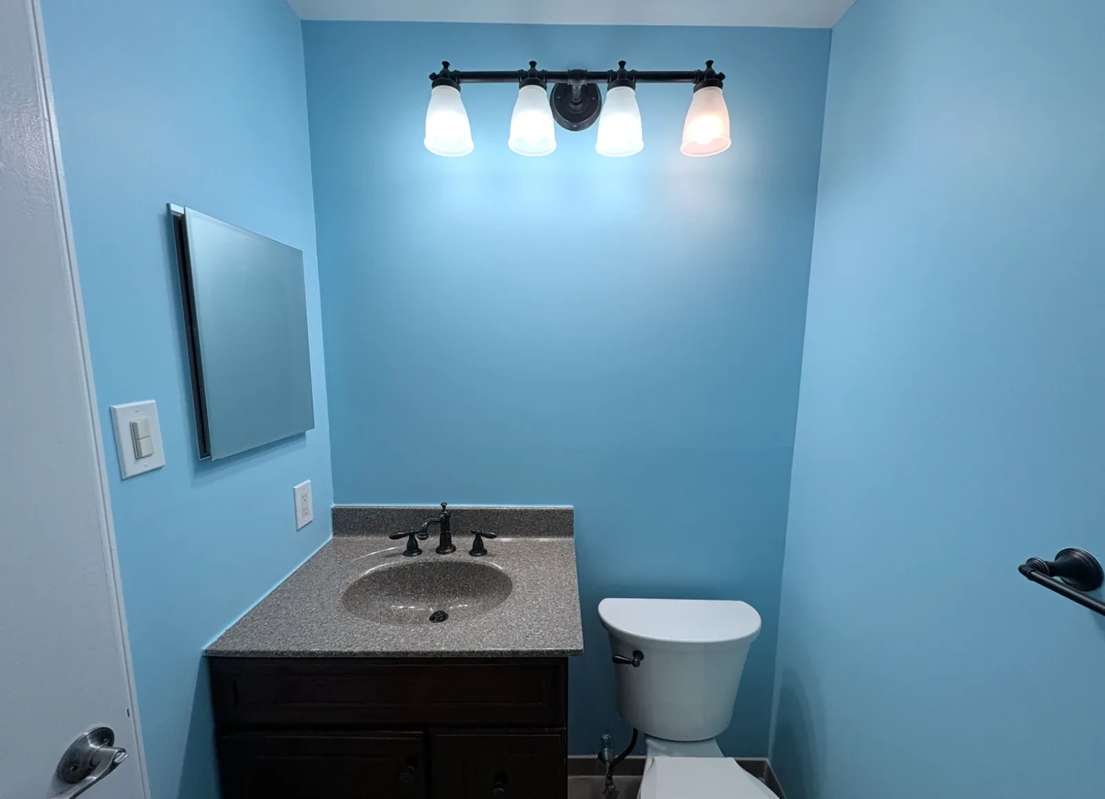 Powder room painted sky blue with white trim, dark wood vanity, and toilet