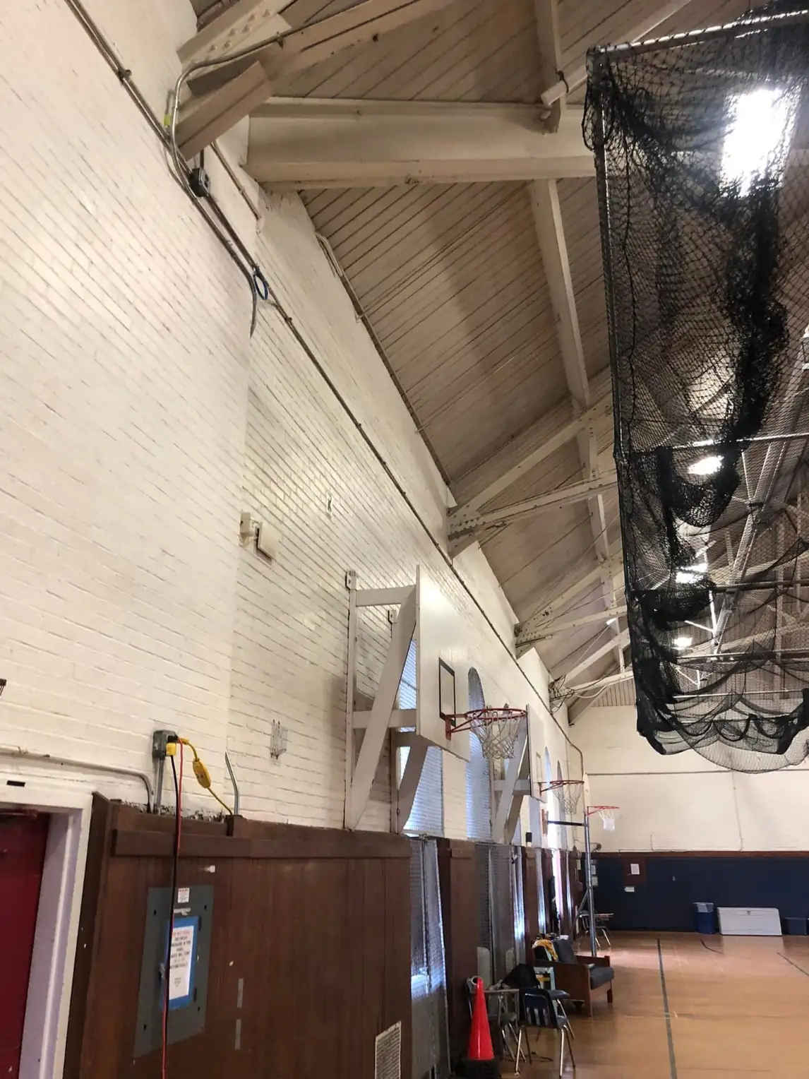 Gymnasium side wall of painted brick before repainting, yellowed and marked up with exposed conduit above dark wainscot