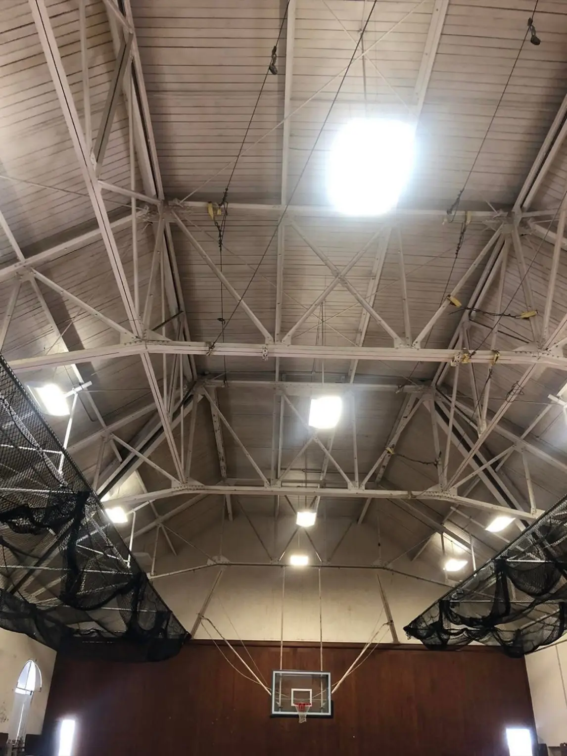 Gymnasium ceiling and steel trusses before painting, dulled and discolored above the basketball hoop