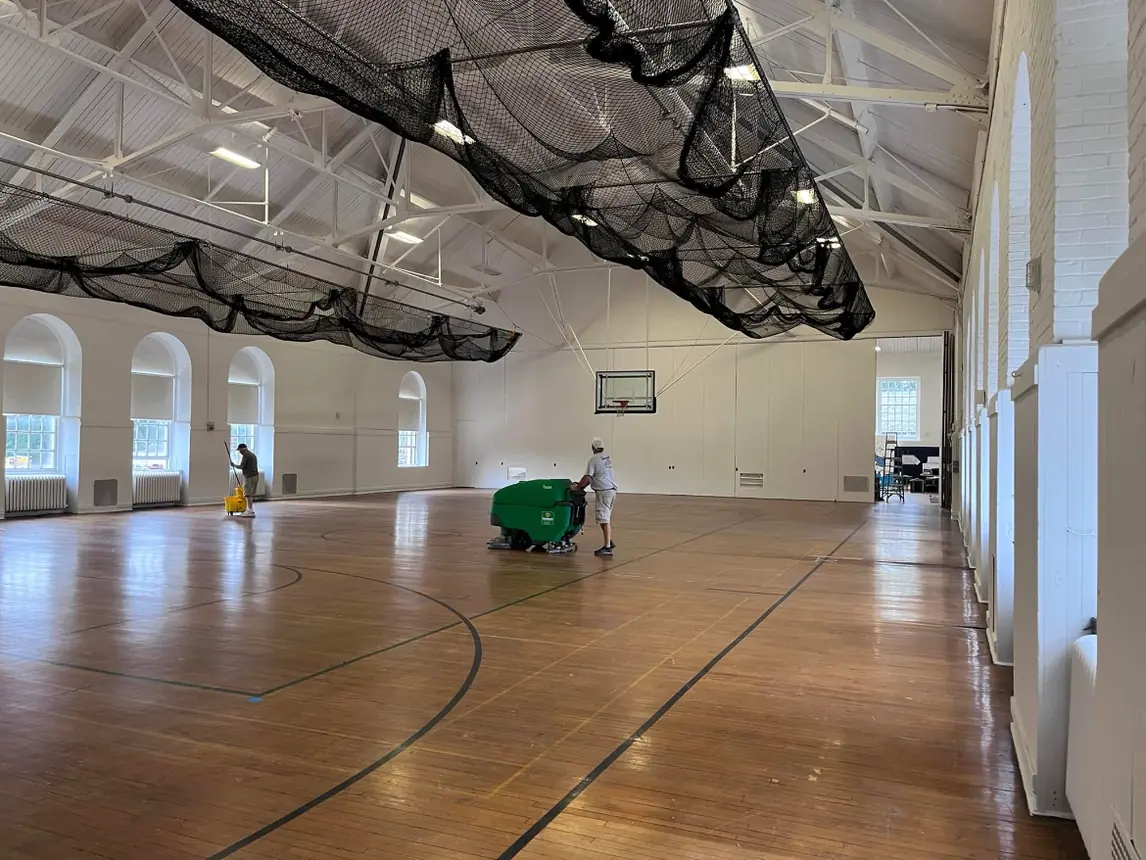 Crew running a floor scrubber across the gymnasium floor after the repaint was finished