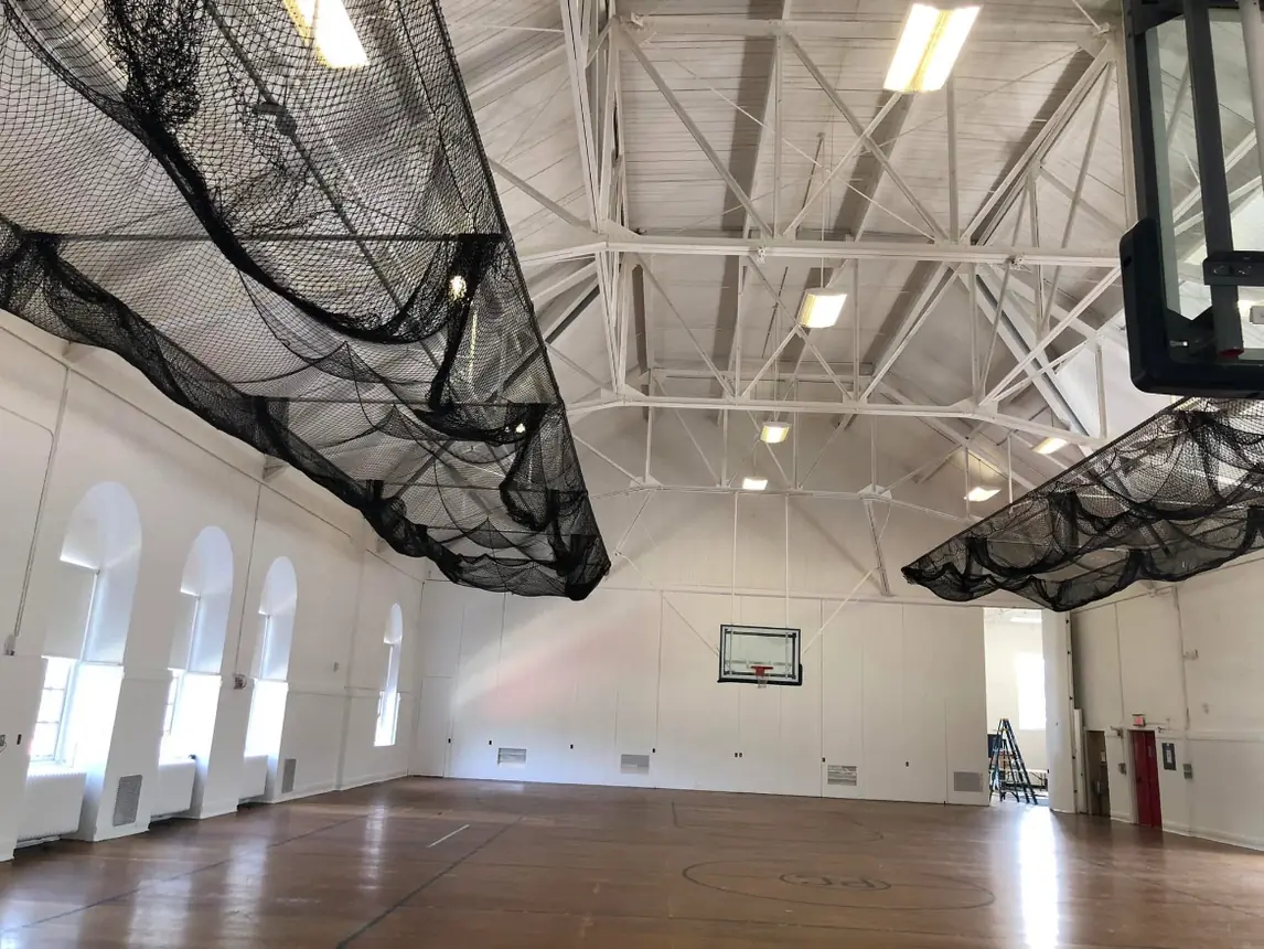 Finished gymnasium with white walls, white ceiling and trusses, and repainted arched windows along the side wall