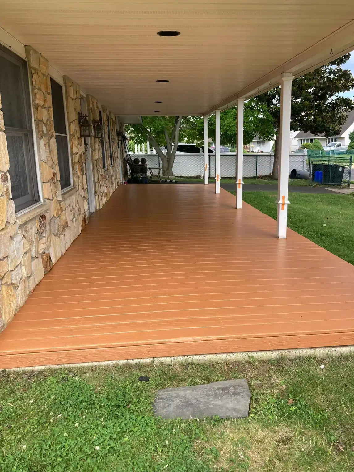 The same covered porch with decking refinished in a solid terracotta and freshly painted white columns
