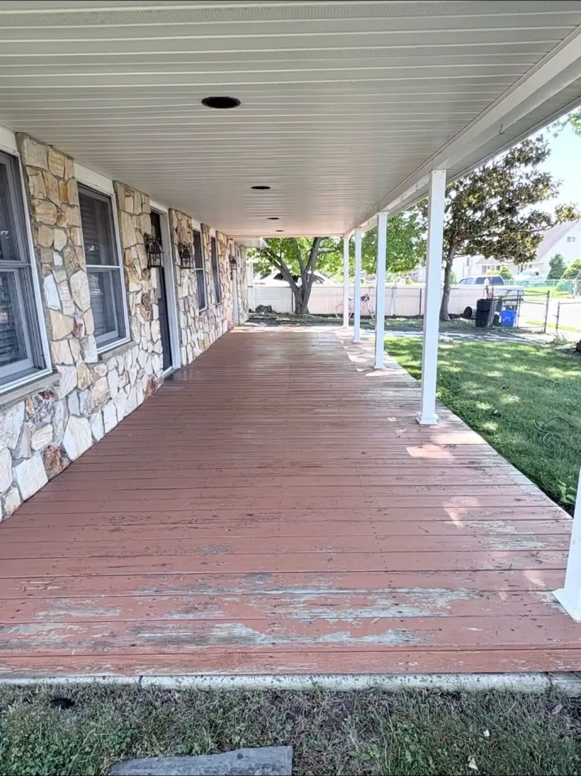 Covered front porch with faded red decking peeling down to bare wood through the middle of the walkway